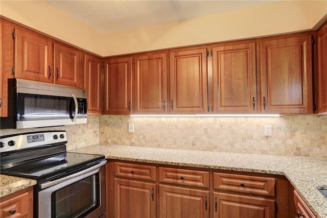 kitchen with appliances with stainless steel finishes, light stone counters, and backsplash