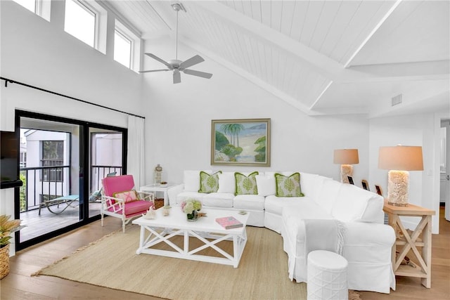 living room featuring a towering ceiling, ceiling fan, beam ceiling, and light hardwood / wood-style flooring