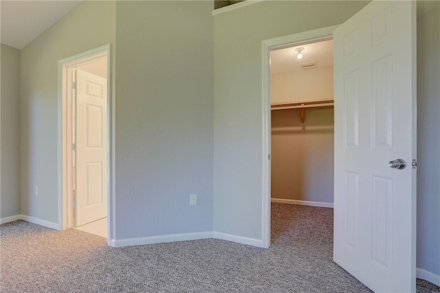 unfurnished bedroom featuring a walk in closet, visible vents, baseboards, and carpet floors