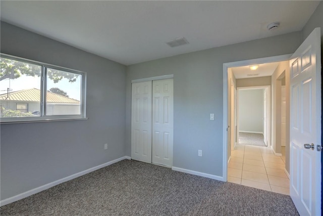 unfurnished bedroom with visible vents, baseboards, light carpet, light tile patterned floors, and a closet