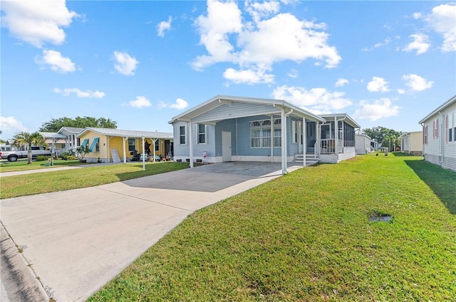 1218 Chipewa Dr, Sebastian, FL 32976 - manufactured / mobile home with concrete driveway, an attached carport, a front yard, and a sunroom