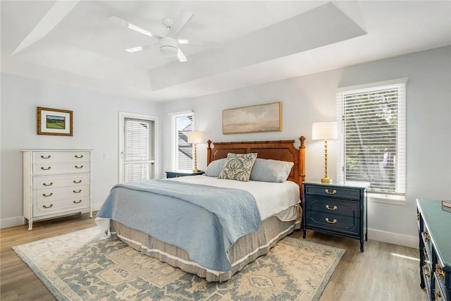 bedroom featuring a tray ceiling, light wood-style flooring, multiple windows, and baseboards