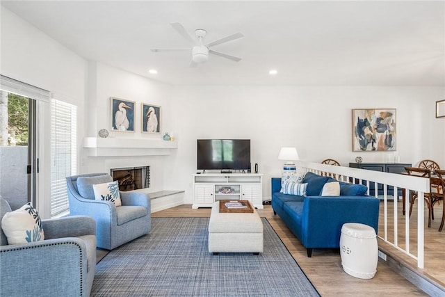 living area with recessed lighting, a fireplace with raised hearth, wood finished floors, and a ceiling fan