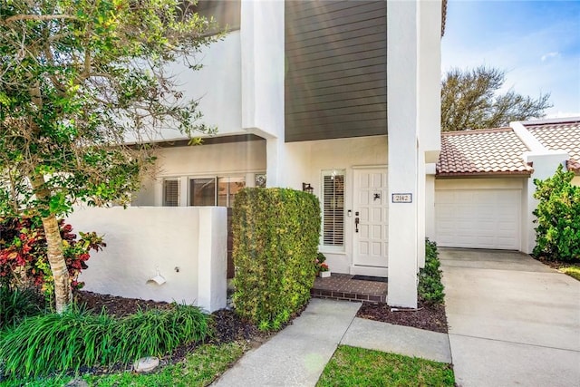 property entrance with an attached garage, driveway, and stucco siding