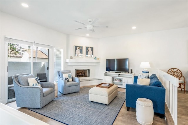 living room featuring recessed lighting, wood finished floors, a fireplace with raised hearth, and ceiling fan