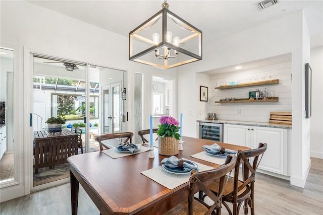 dining room featuring beverage cooler, visible vents, an inviting chandelier, a bar, and light wood-type flooring