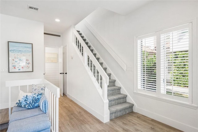 stairs with plenty of natural light, wood finished floors, visible vents, and baseboards