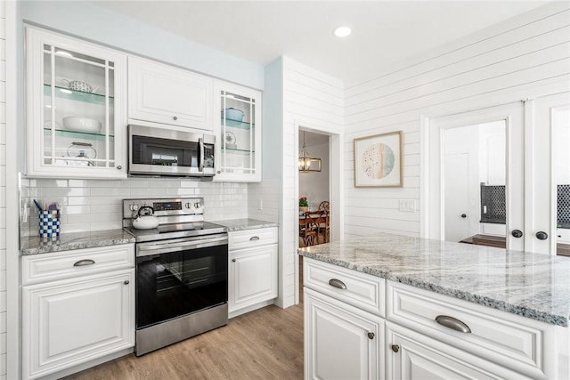 kitchen with light wood finished floors, backsplash, light stone counters, stainless steel appliances, and white cabinetry