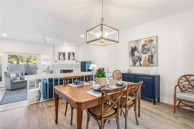 dining area with recessed lighting, light wood-style flooring, a fireplace, and ceiling fan with notable chandelier