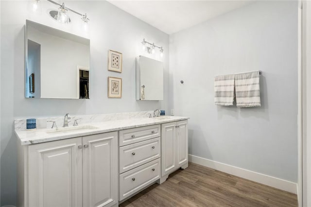 bathroom featuring double vanity, wood finished floors, baseboards, and a sink