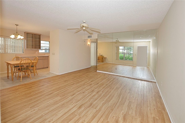 unfurnished living room with light wood-type flooring, ceiling fan with notable chandelier, and a textured ceiling