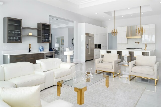 living room featuring a raised ceiling, beverage cooler, a notable chandelier, and indoor wet bar