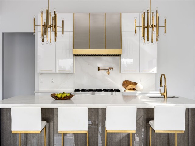 kitchen with a kitchen bar, white cabinetry, sink, and gas cooktop