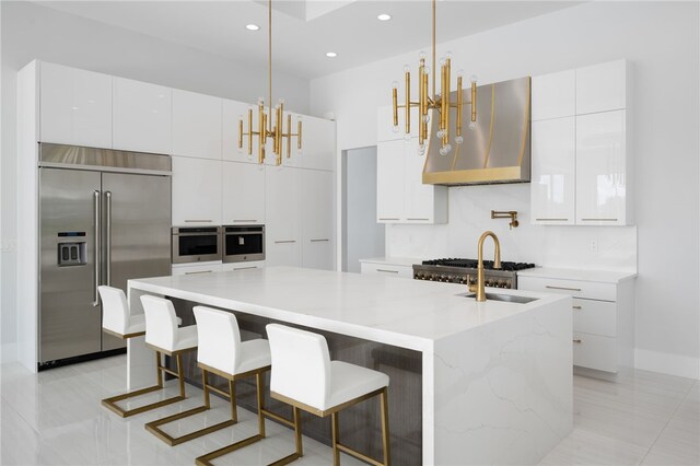 kitchen with pendant lighting, ventilation hood, an island with sink, and appliances with stainless steel finishes