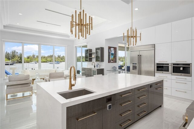 kitchen featuring decorative light fixtures, stainless steel appliances, a raised ceiling, and an island with sink