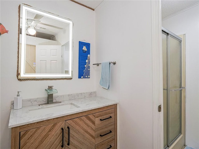 bathroom featuring ceiling fan, vanity, a shower with door, and a textured ceiling