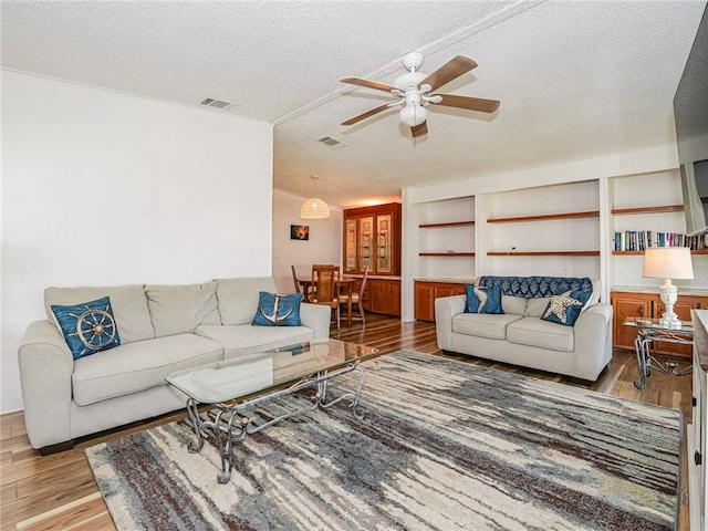 living room featuring ceiling fan, light hardwood / wood-style flooring, and a textured ceiling