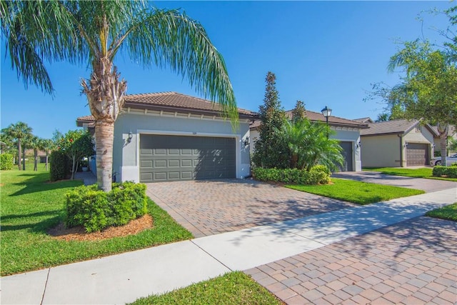 view of front facade featuring stucco siding, a front lawn, a garage, a tile roof, and decorative driveway