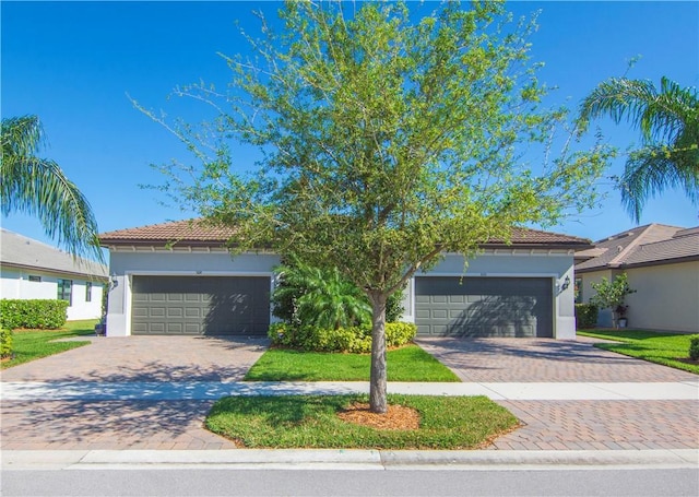 view of front of house with decorative driveway, a garage, a tile roof, and stucco siding