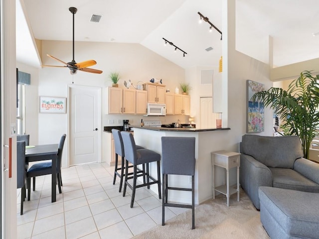 kitchen with vaulted ceiling, a kitchen bar, ceiling fan, kitchen peninsula, and light brown cabinetry