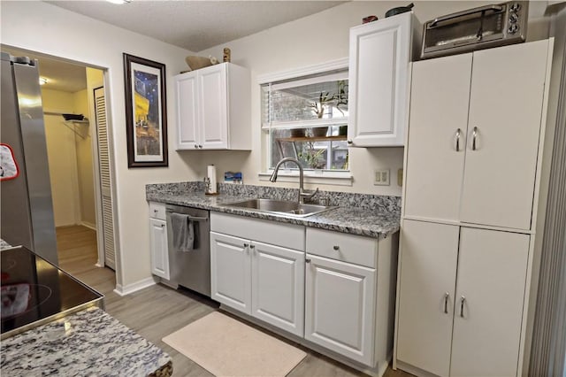 kitchen featuring sink, light stone counters, appliances with stainless steel finishes, white cabinets, and light wood-type flooring