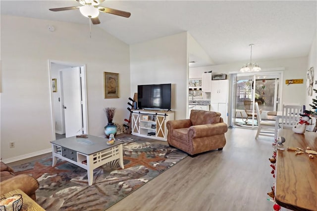 living room featuring hardwood / wood-style flooring, ceiling fan with notable chandelier, and vaulted ceiling