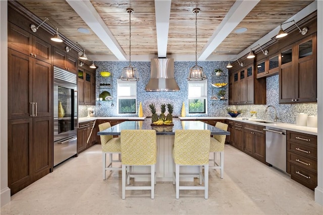 kitchen featuring beamed ceiling, appliances with stainless steel finishes, a kitchen island, and wall chimney range hood