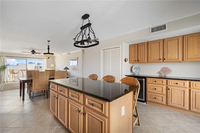 kitchen with a textured ceiling, beverage cooler, decorative light fixtures, a center island, and a breakfast bar area