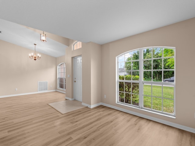 empty room with a chandelier, light hardwood / wood-style floors, and lofted ceiling