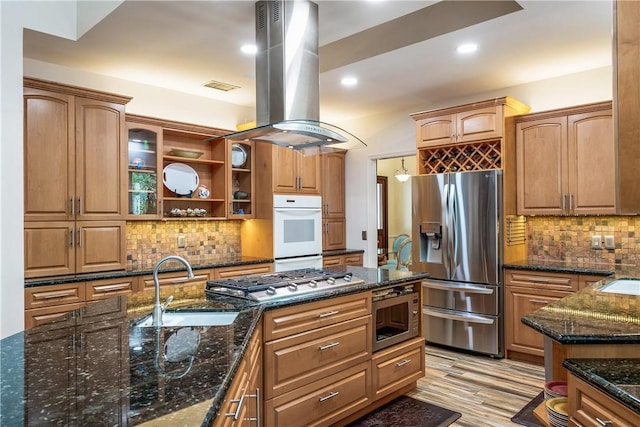 kitchen with dark stone counters, appliances with stainless steel finishes, island exhaust hood, open shelves, and a sink