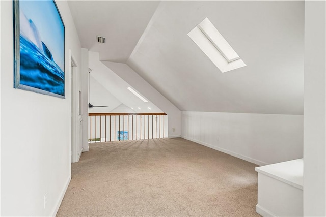 additional living space featuring visible vents, a ceiling fan, carpet flooring, vaulted ceiling with skylight, and baseboards