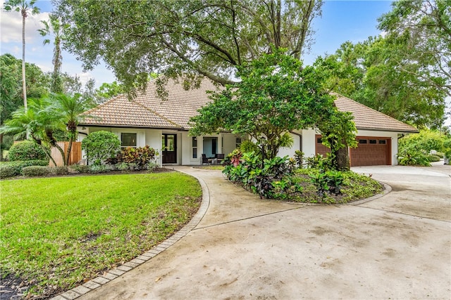 view of front of property with driveway, a tile roof, an attached garage, a front lawn, and stucco siding