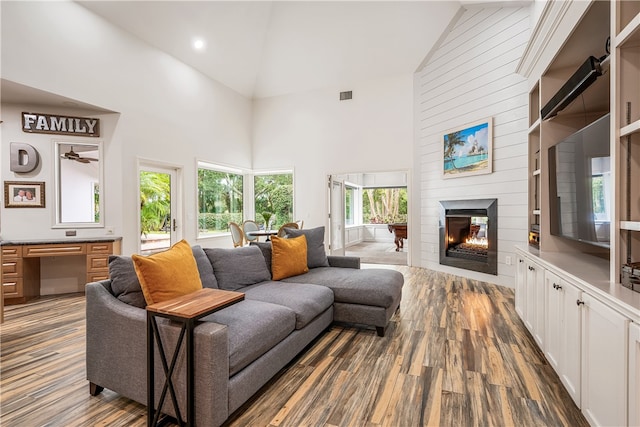 living area featuring visible vents, built in study area, wood finished floors, high vaulted ceiling, and a lit fireplace