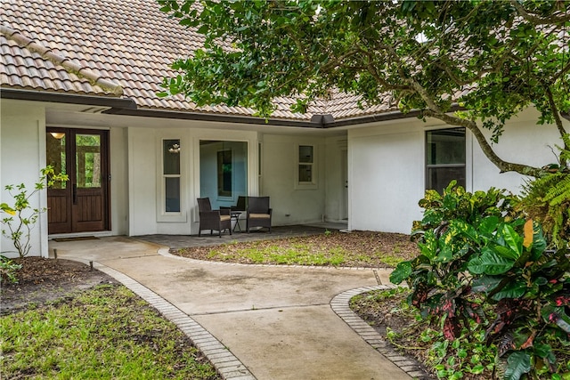 property entrance featuring covered porch, a tiled roof, and stucco siding