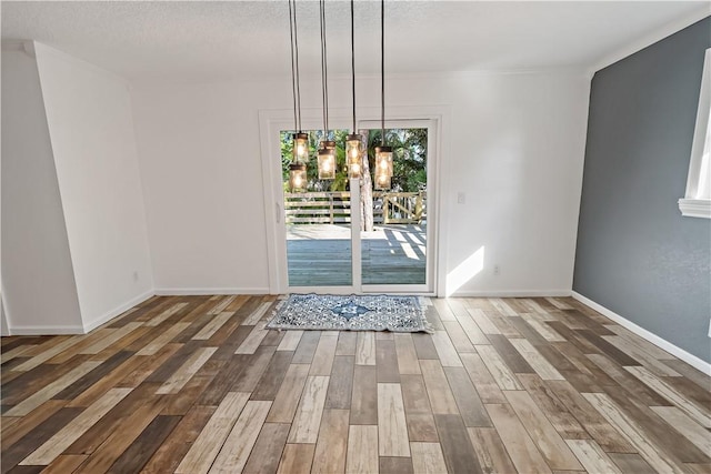 unfurnished dining area featuring a textured ceiling, baseboards, and wood finished floors