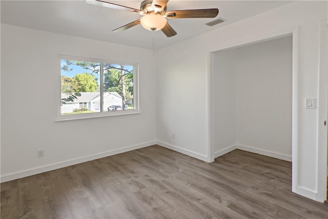 unfurnished room with a ceiling fan, visible vents, wood finished floors, and baseboards