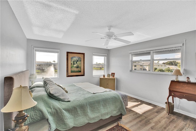 bedroom featuring hardwood / wood-style flooring, multiple windows, a textured ceiling, and ceiling fan