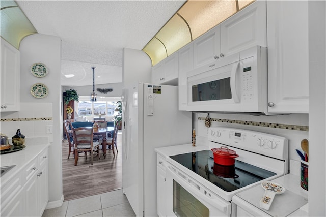 kitchen featuring a textured ceiling, light tile patterned floors, an inviting chandelier, white appliances, and white cabinets