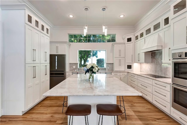 kitchen with stainless steel appliances, light stone counters, a center island, custom exhaust hood, and decorative light fixtures