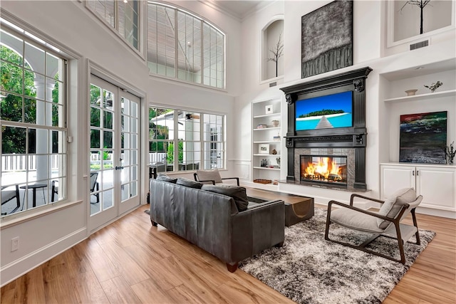 living room with light hardwood / wood-style floors, a towering ceiling, built in shelves, and crown molding