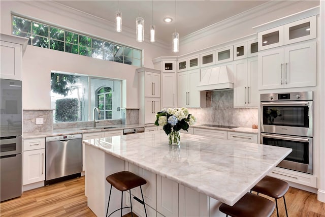 kitchen with stainless steel appliances, a center island, white cabinets, sink, and premium range hood