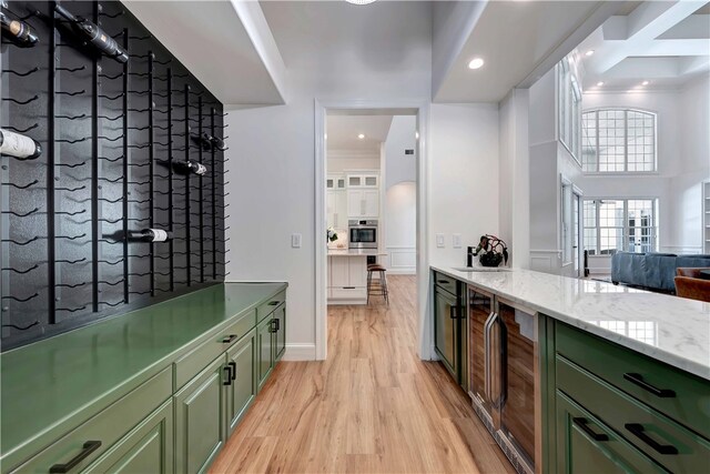 interior space featuring green cabinets, light stone counters, light hardwood / wood-style flooring, crown molding, and stainless steel oven