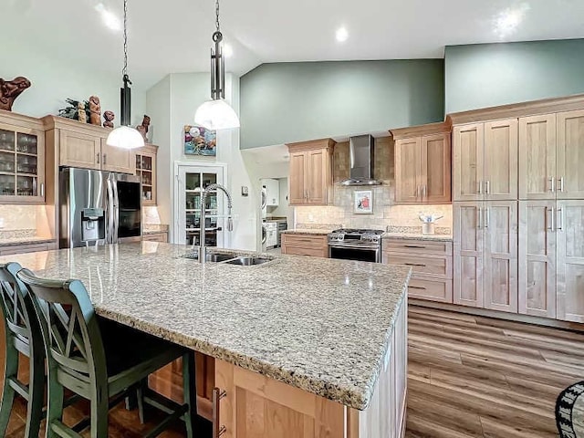 kitchen with wall chimney range hood, sink, a large island, and appliances with stainless steel finishes