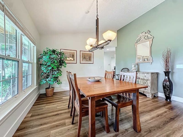 dining space featuring wood-type flooring, a healthy amount of sunlight, an inviting chandelier, and lofted ceiling