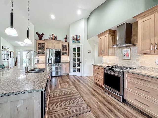 kitchen with appliances with stainless steel finishes, decorative light fixtures, sink, light hardwood / wood-style floors, and wall chimney exhaust hood