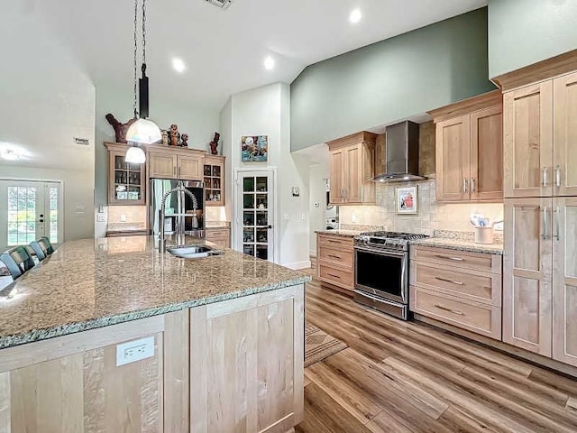 kitchen featuring a spacious island, wall chimney range hood, appliances with stainless steel finishes, light brown cabinets, and light hardwood / wood-style flooring