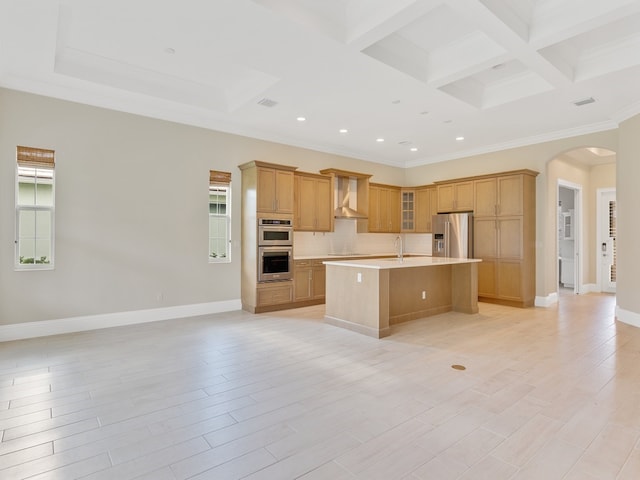 kitchen featuring appliances with stainless steel finishes, a kitchen island with sink, coffered ceiling, wall chimney range hood, and light wood-type flooring