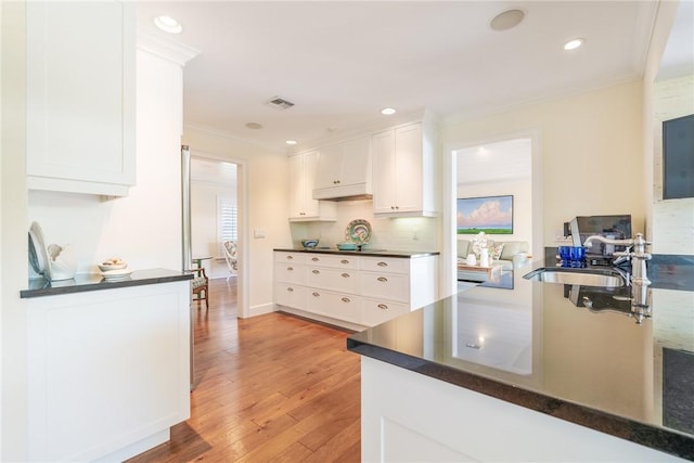 kitchen with dark countertops, visible vents, light wood finished floors, crown molding, and white cabinets