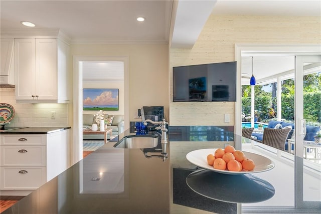 kitchen featuring a sink, white cabinets, crown molding, dark countertops, and backsplash