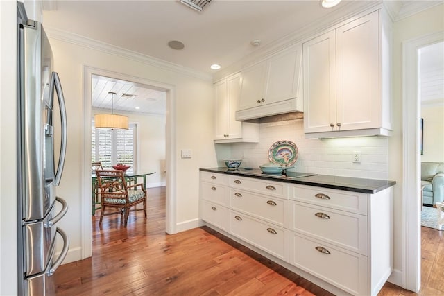 kitchen featuring crown molding, light wood-style floors, stainless steel refrigerator with ice dispenser, dark countertops, and backsplash